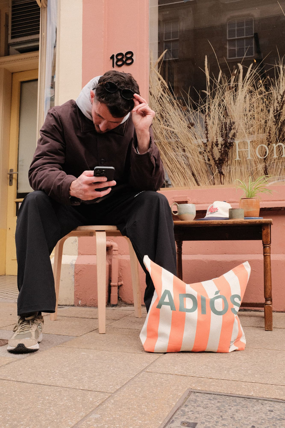 Man sitting on a stool using a phone with a 'Adiós' tote bag nearby.