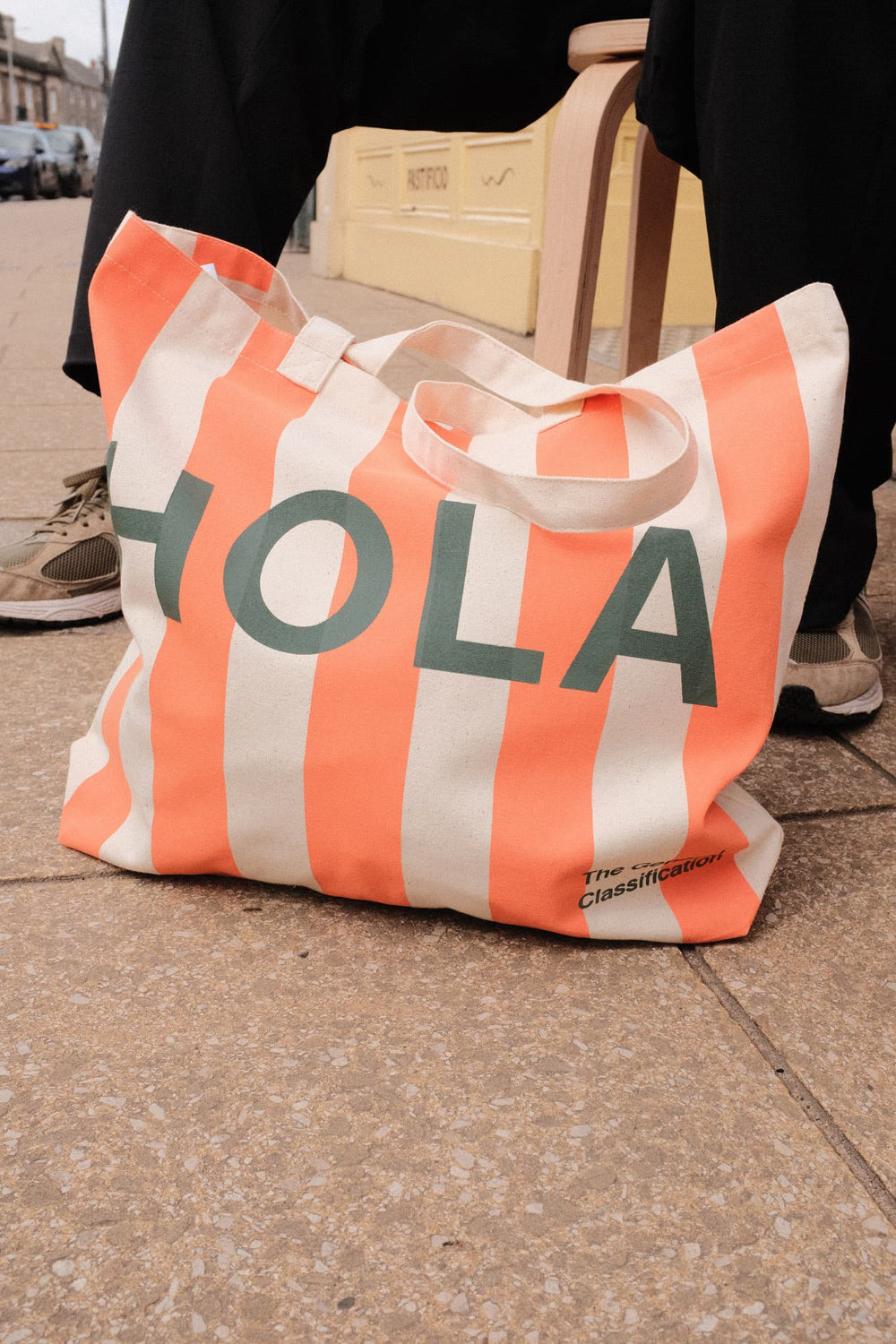 Orange and white striped bag with 'HOLA' text on a pavement.