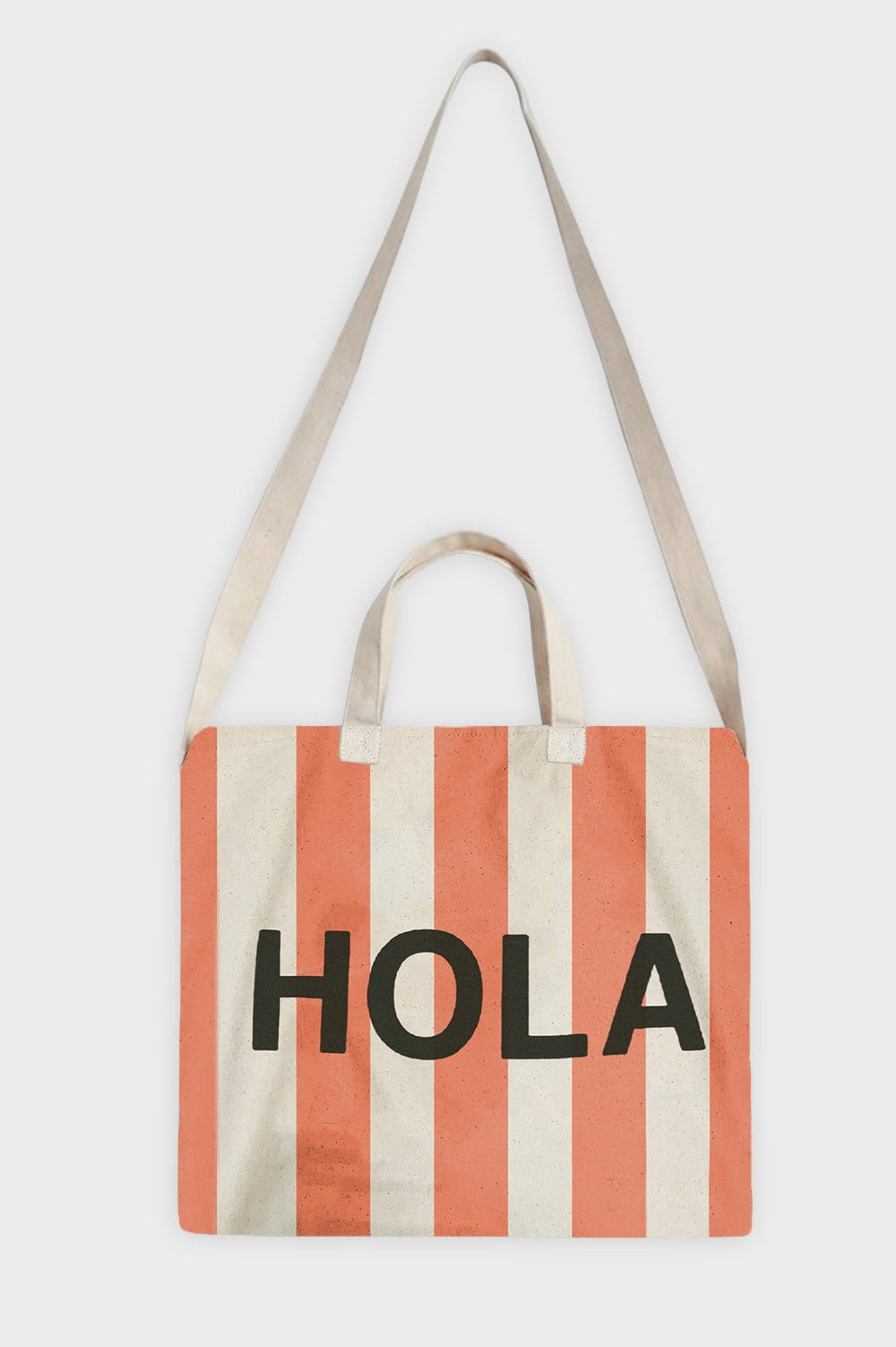 A canvas tote bag with vertical coral pink and cream stripes, featuring the word 'HOLA' printed in bold black letters across the front. It has two cream fabric shoulder straps and two short cream top handles, shown against a plain light gray background.