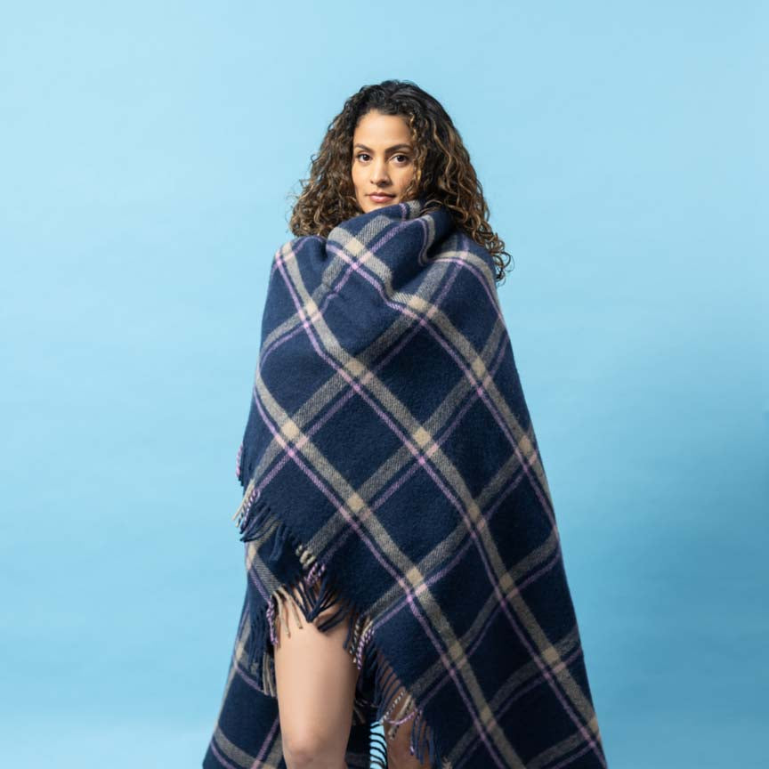 Woman wrapped in a navy and beige plaid blanket against a light blue background