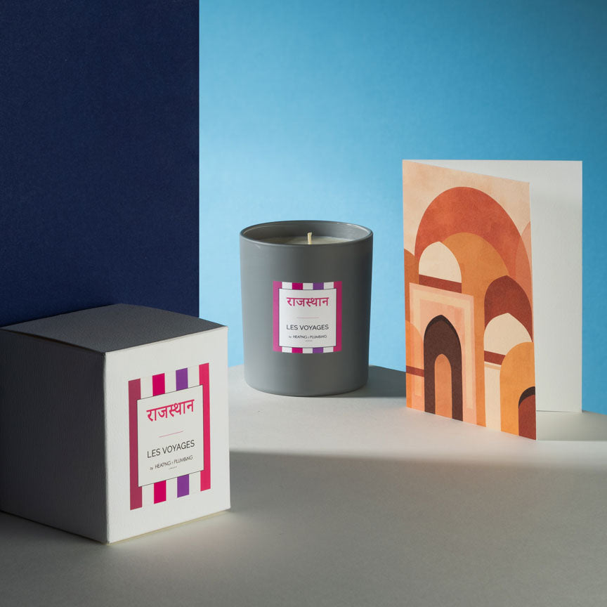 Candle and packaging with a colourful card on a blue and grey background