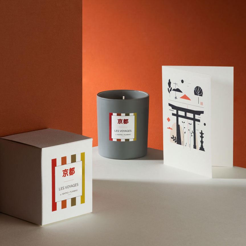 Grey candle with a decorative label next to a white box and card on an orange background