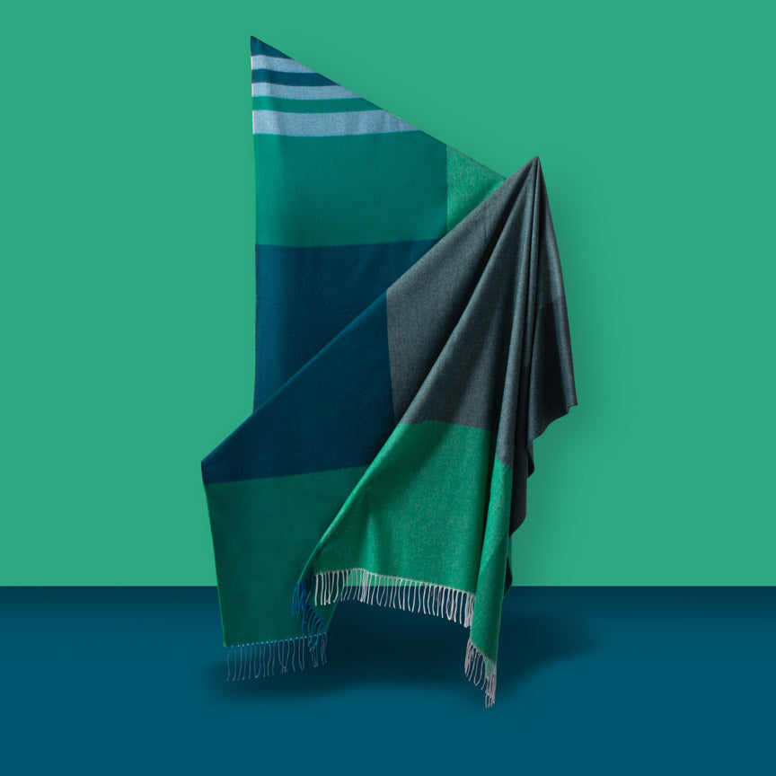Colour-blocked blanket with geometric pattern on a green and blue gradient background