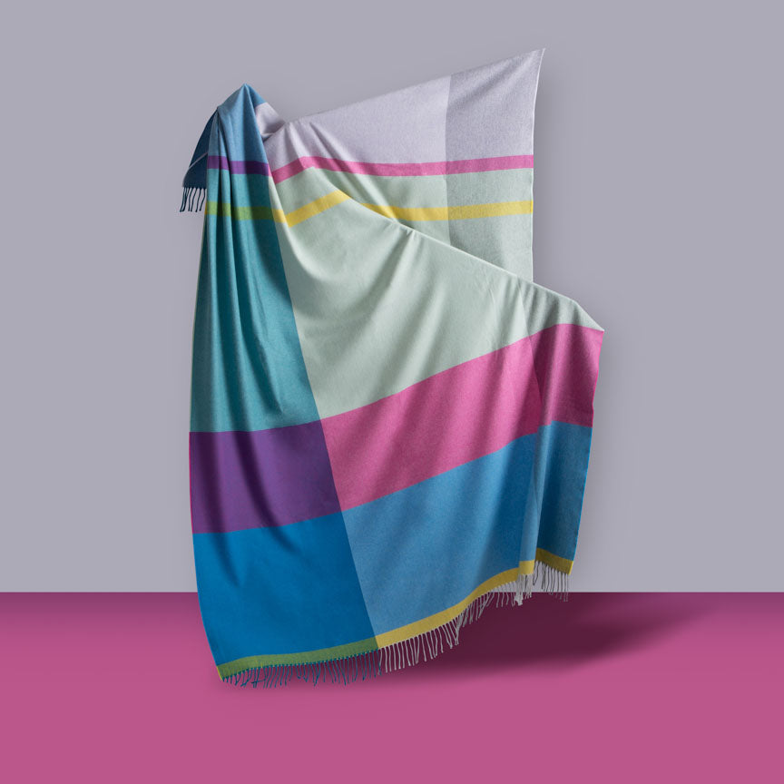Colorful striped blanket draped over a surface with a grey and pink background