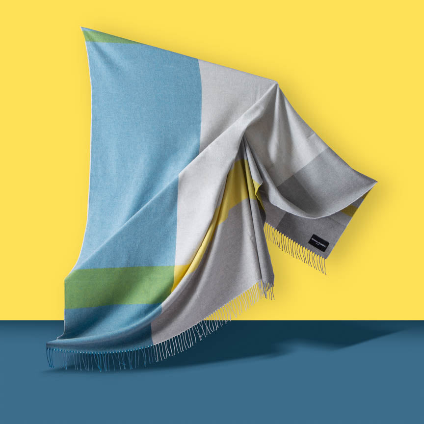 Colourful blanket with geometric pattern on a yellow and blue gradient background