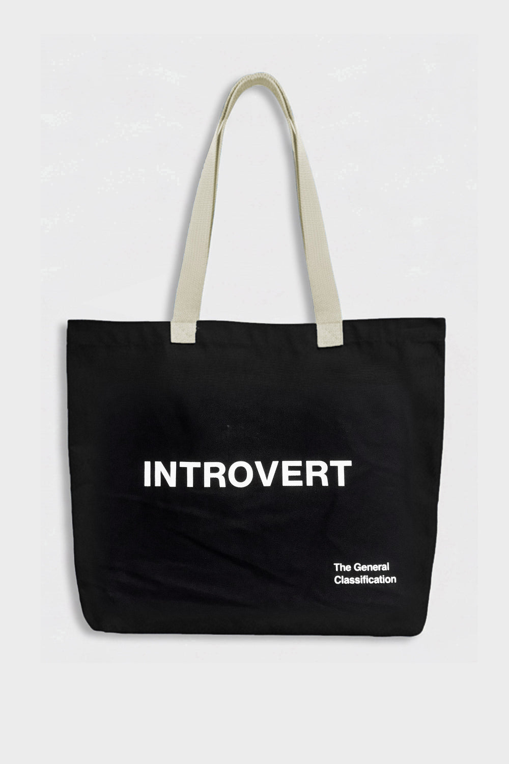 A black canvas tote bag with cream-colored shoulder straps, featuring the word 'INTROVERT' printed in bold white capital letters on the front, with smaller text below reading 'The General Classification'.