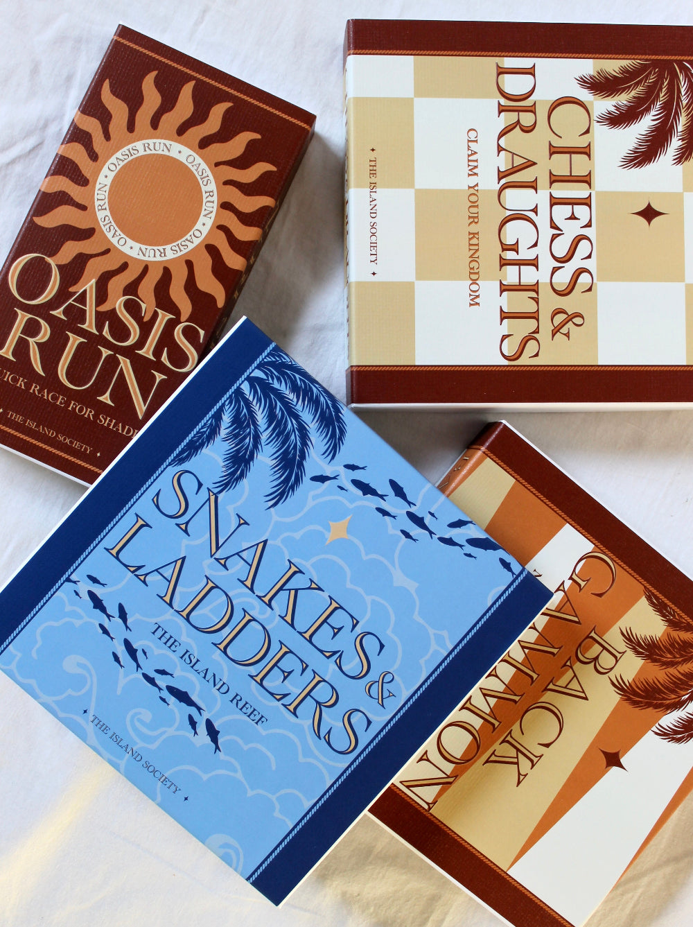 Blue Island Reef Snakes and Ladders box photographed alongside other illustrated board games from The Island Society.