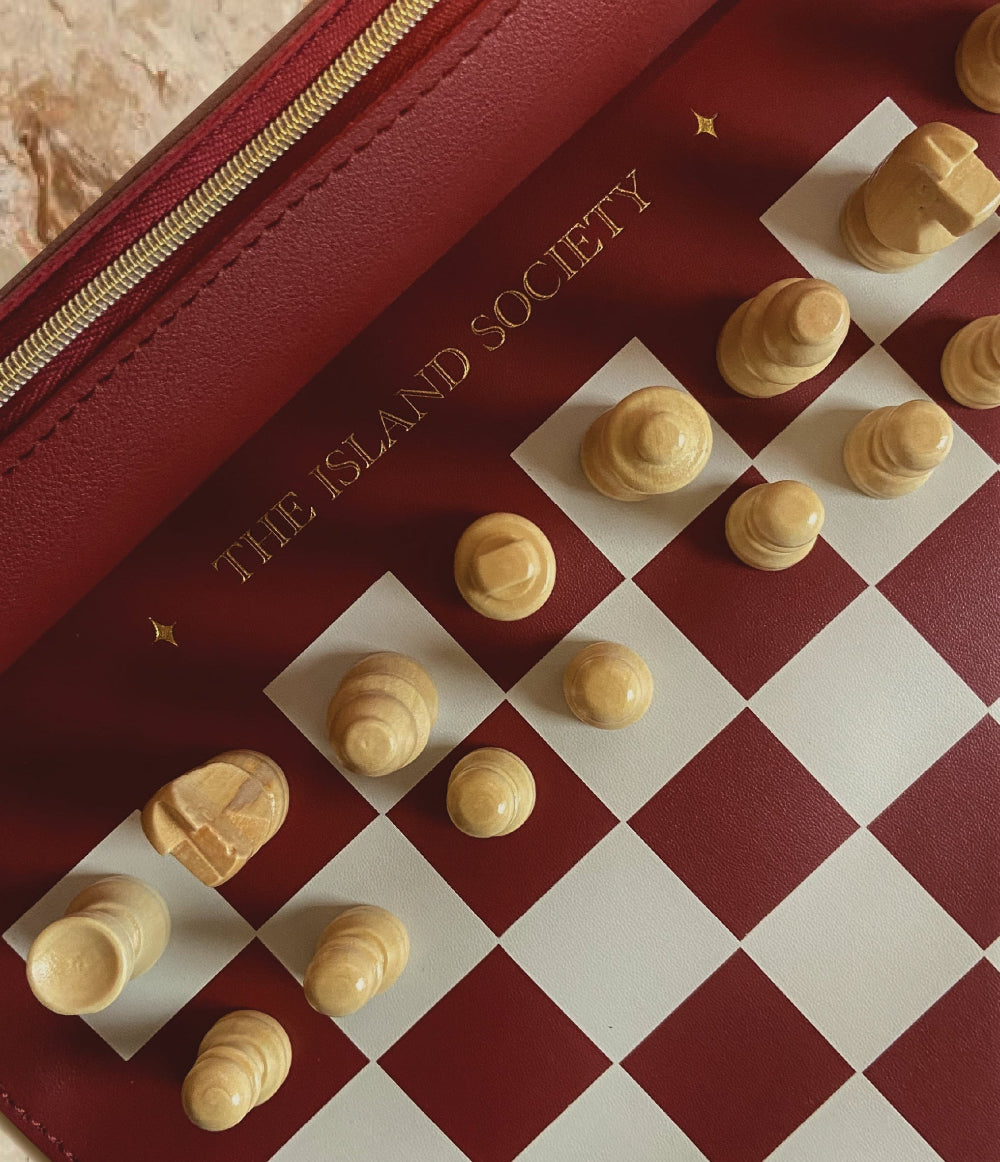 The Island Society luxury travel chess set with burgundy chess board and wooden pieces displayed on a table.