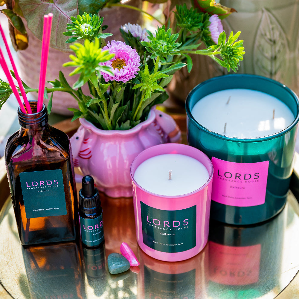 Lords fragrance products including candles and diffusers on a reflective surface with flowers in the background.