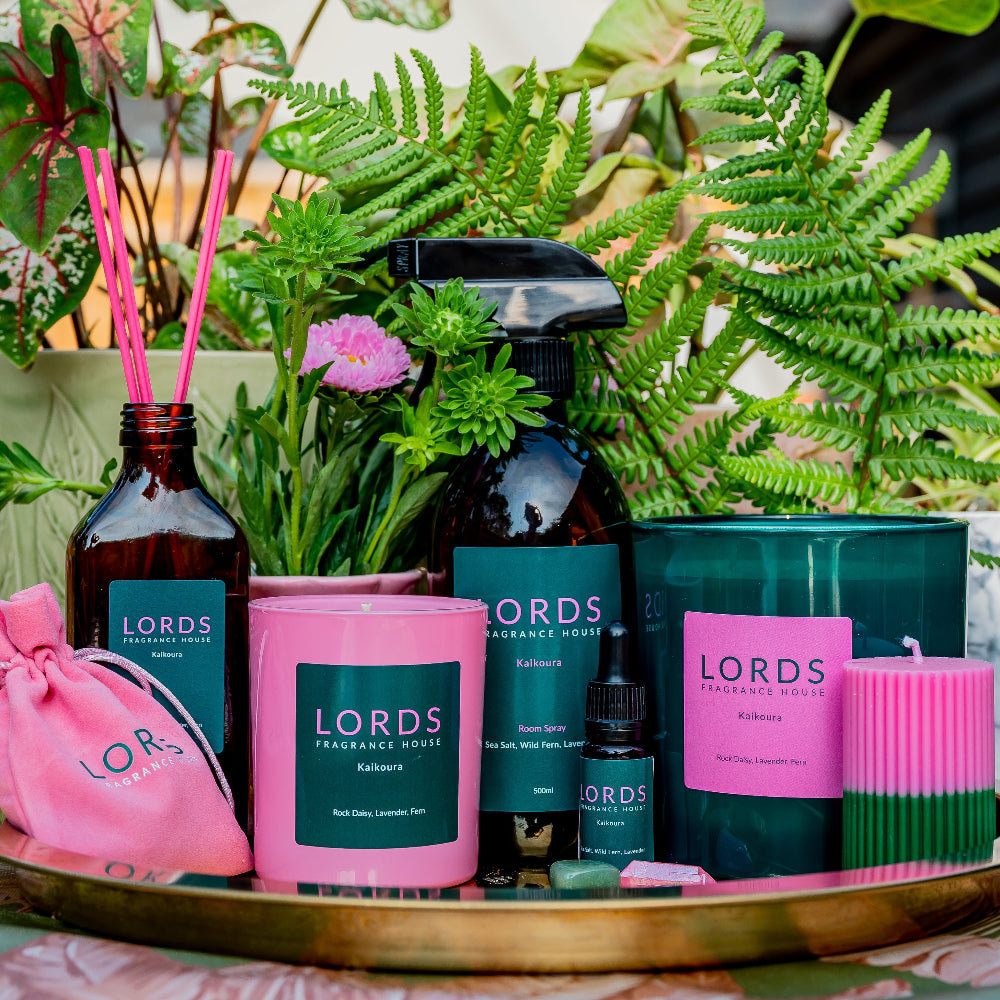 Assorted Lords Fragrance House products including candles, diffusers, and bottles on a table with plants in the background.