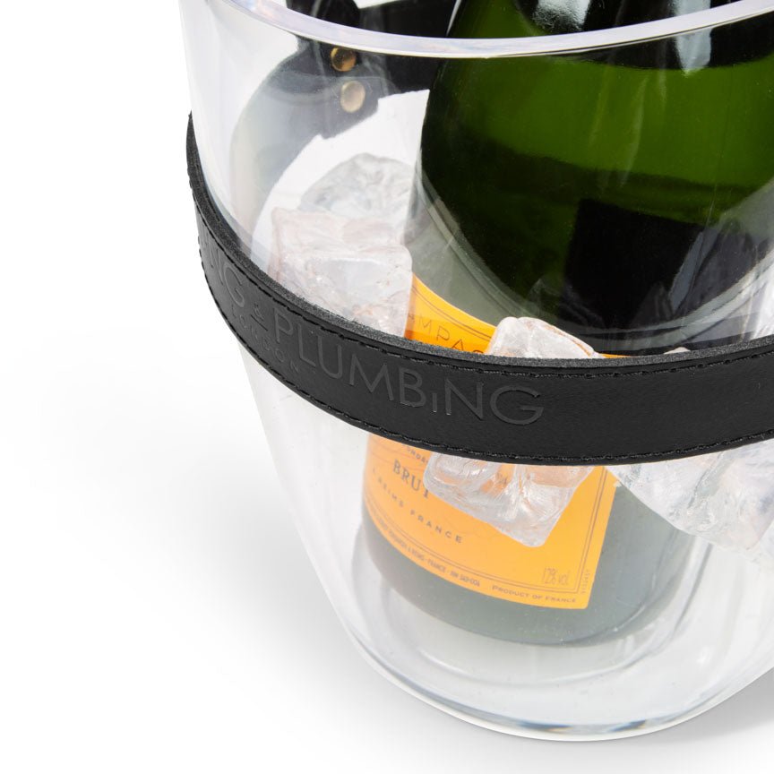 Bottle of champagne in a clear ice bucket with a black band labeled 'HEATING AND PLUMBING'.