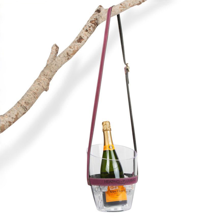 Champagne bottle in a clear holder with purple strap against a white background