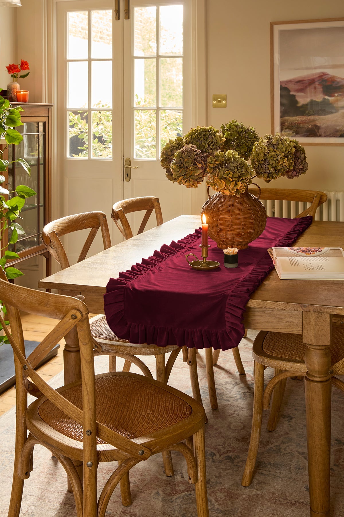 Dining room with wooden table and chairs, burgandy ruffled table runner, and decorative items.