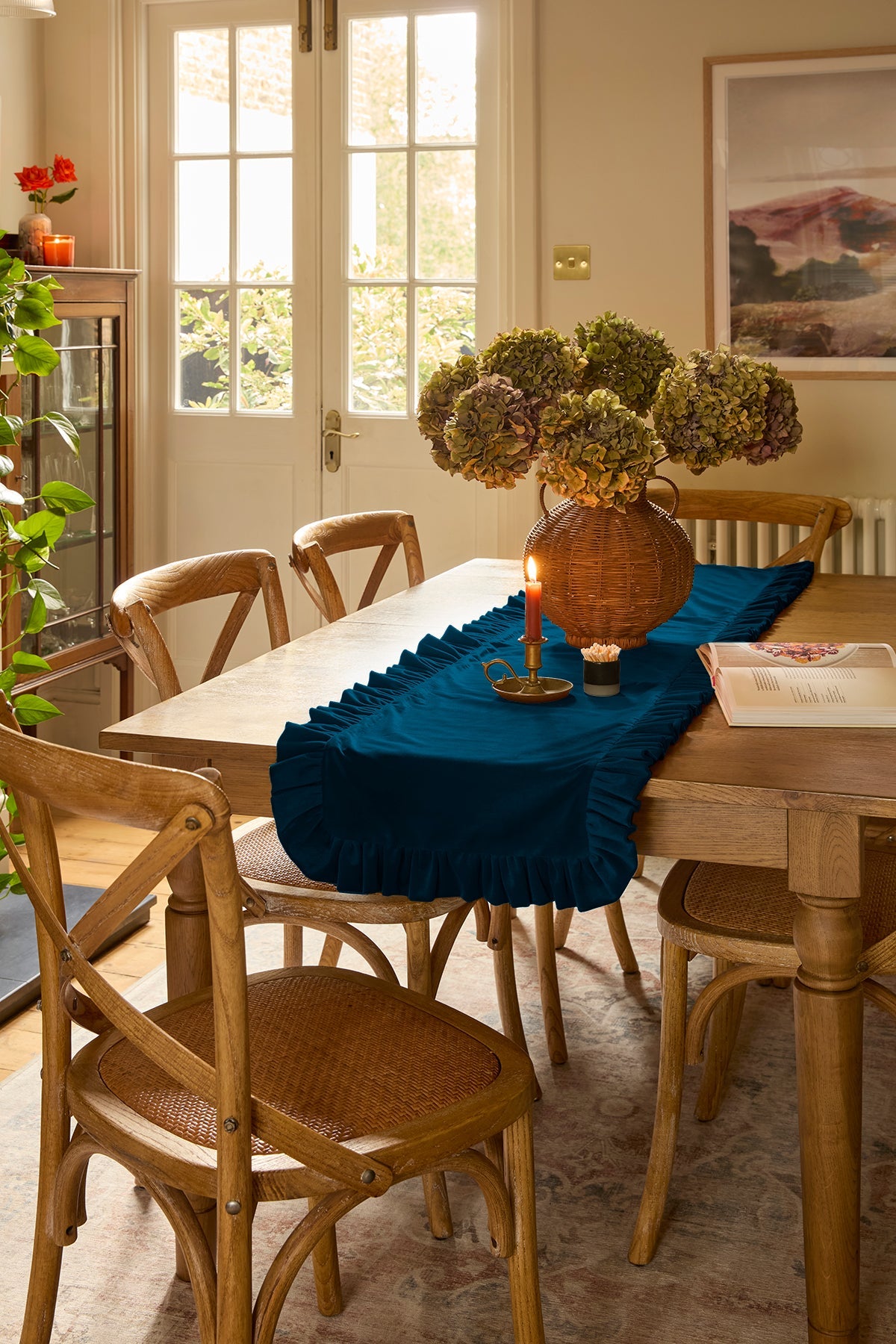 Dining room with wooden table and chairs, teal velvet table runner, and decorative items.
