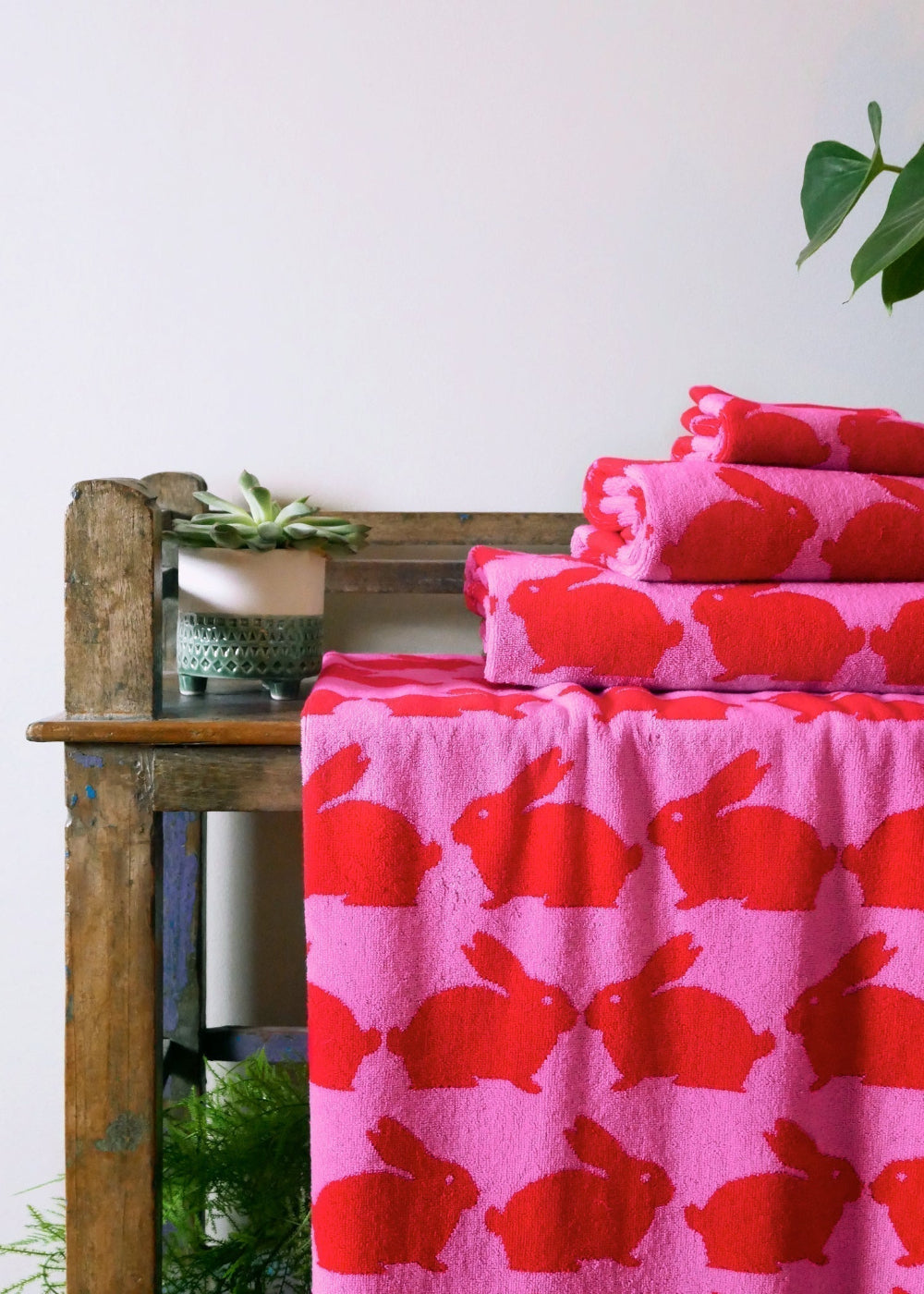 Pink towels with red bunny pattern on a wooden table against a white wall.