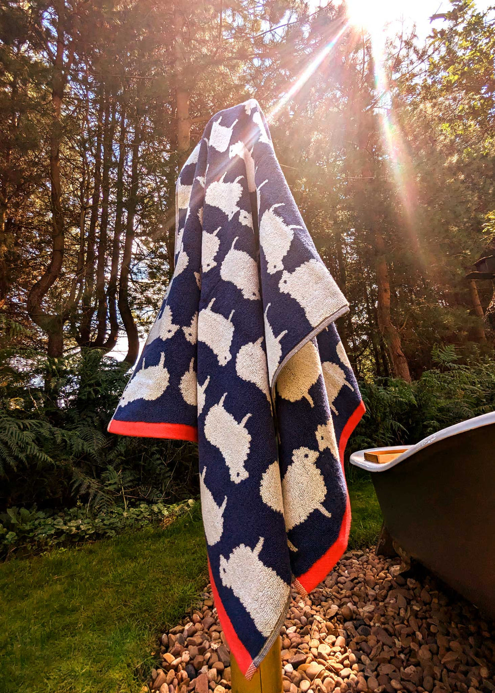 Navy bath towel with white sheep pattern draped over a garden bench with trees in the background