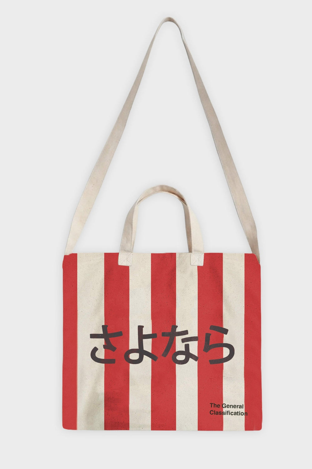 A canvas tote bag with vertical red and cream stripes, featuring black Japanese text across the front and the brand name 'The General Classification' in the bottom right corner. The bag has cream-colored shoulder straps and handles, set against a plain light grey background.