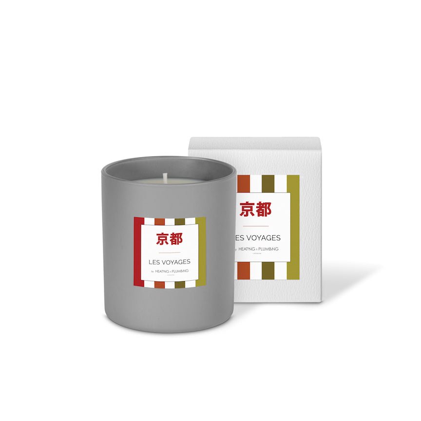 Grey candle with a decorative label next to its packaging on a white background