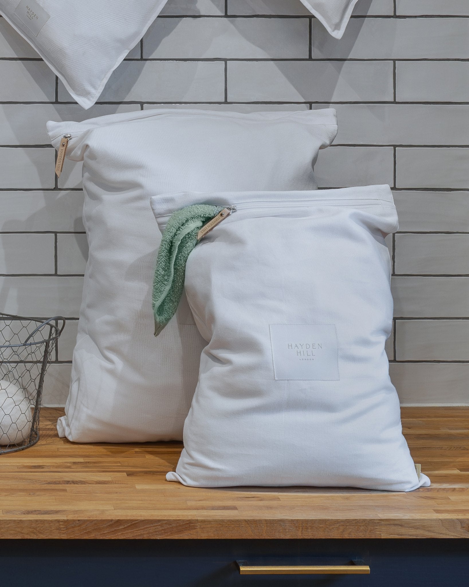 White laundry bags with drawstrings on a wooden surface against a tiled wall background.