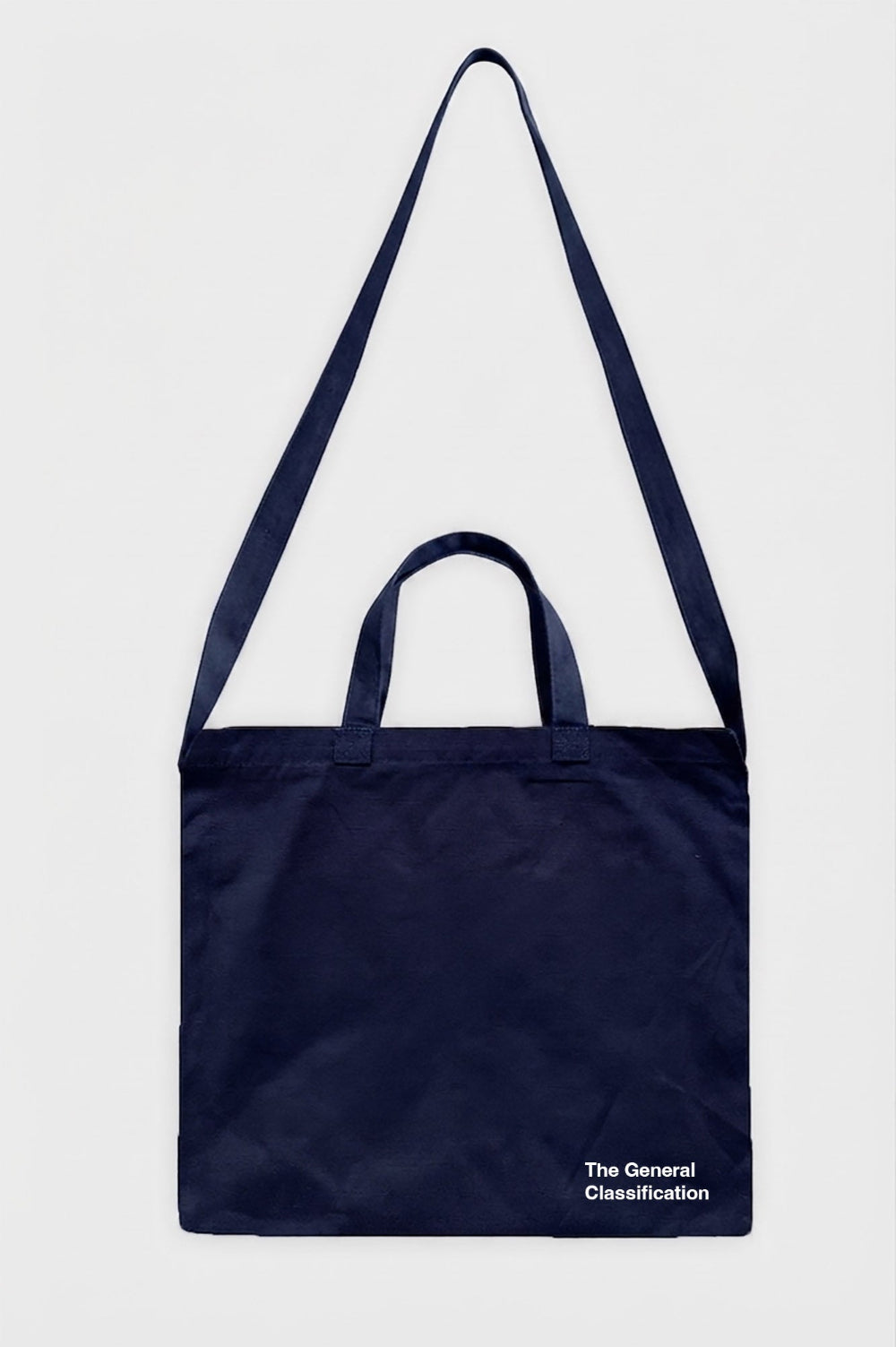 A navy blue canvas tote bag with dual top handles and a long shoulder strap, featuring the white printed text 'The General Classification' on the bottom right, shown against a light grey background.