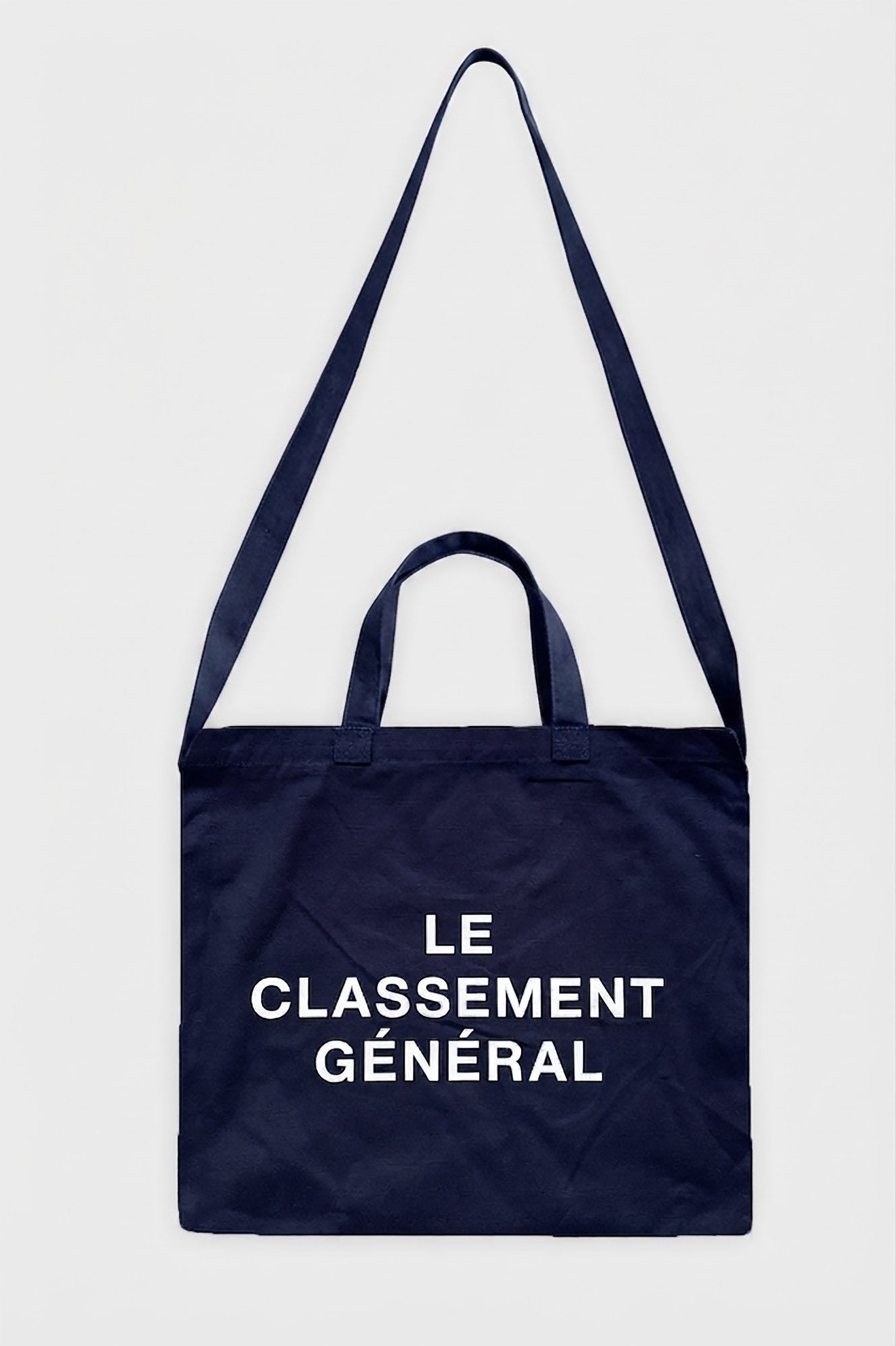 A navy blue canvas tote bag with white printed text reading 'LE CLASSEMENT GÉNÉRAL' on the front, shown against a plain light grey background.