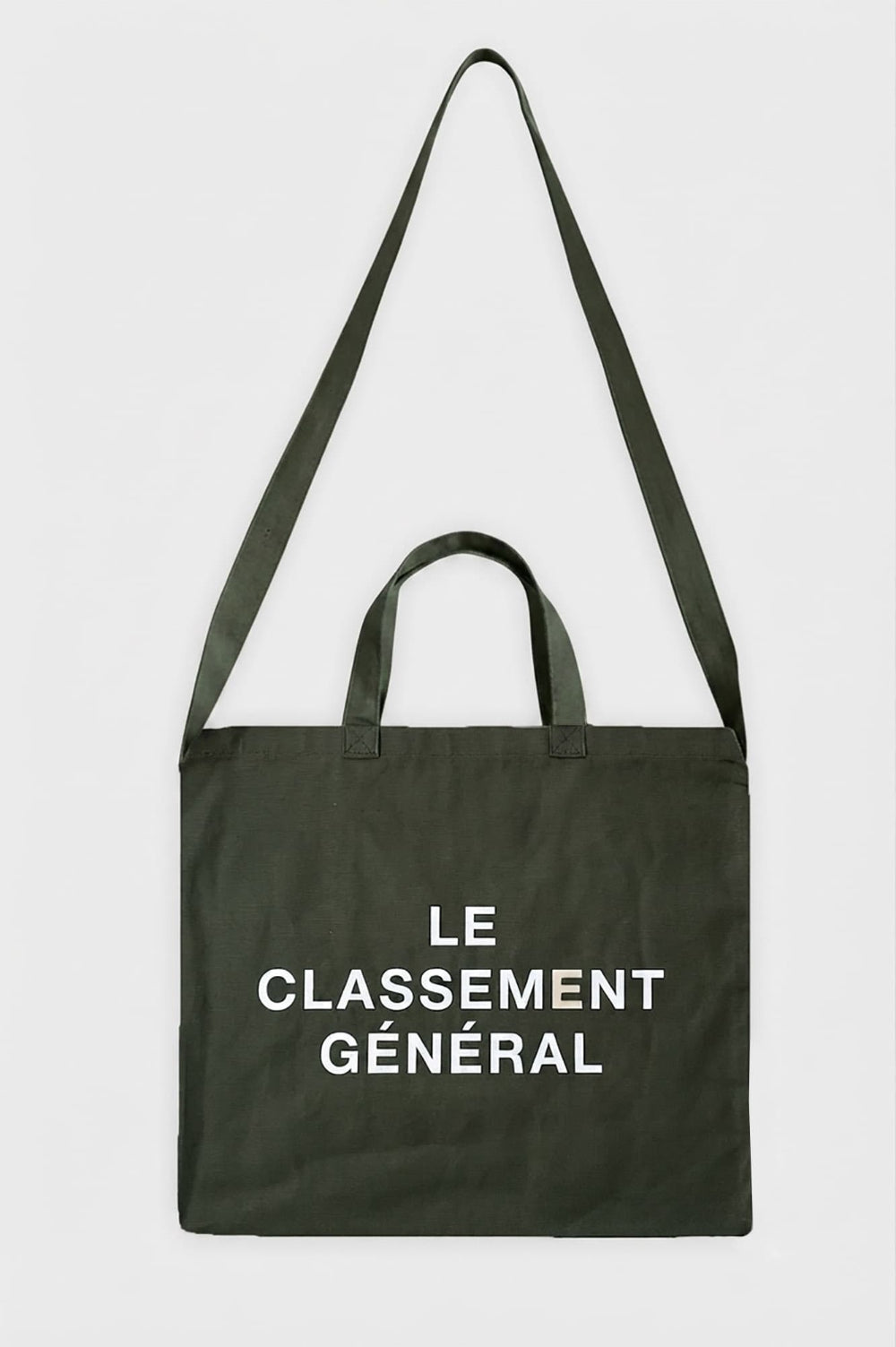 An olive green canvas tote bag with two top handles and a long shoulder strap, featuring the white printed French text 'LE CLASSEMENT GÉNÉRAL' on the front, set against a plain light gray background.
