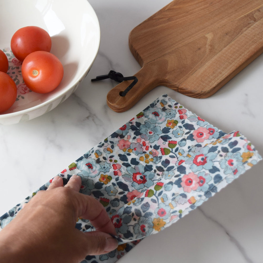 Floral-patterned beeswax wrap on a marble surface with tomatoes and a cutting board.
