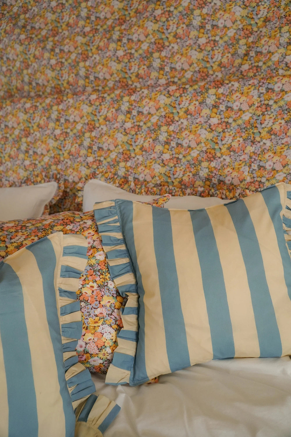 Striped pillows with floral bedding against a floral wall.