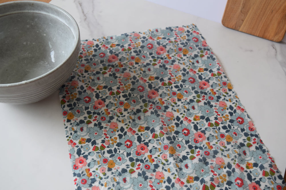Floral-patterned liberty beeswax wrap on a white surface with a bowl and wooden board.