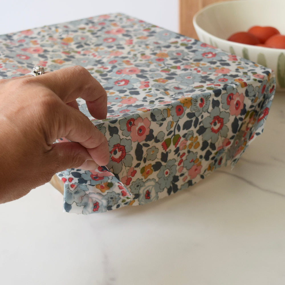 Floral-patterned fabric-covered box with a hand opening it on a light surface.