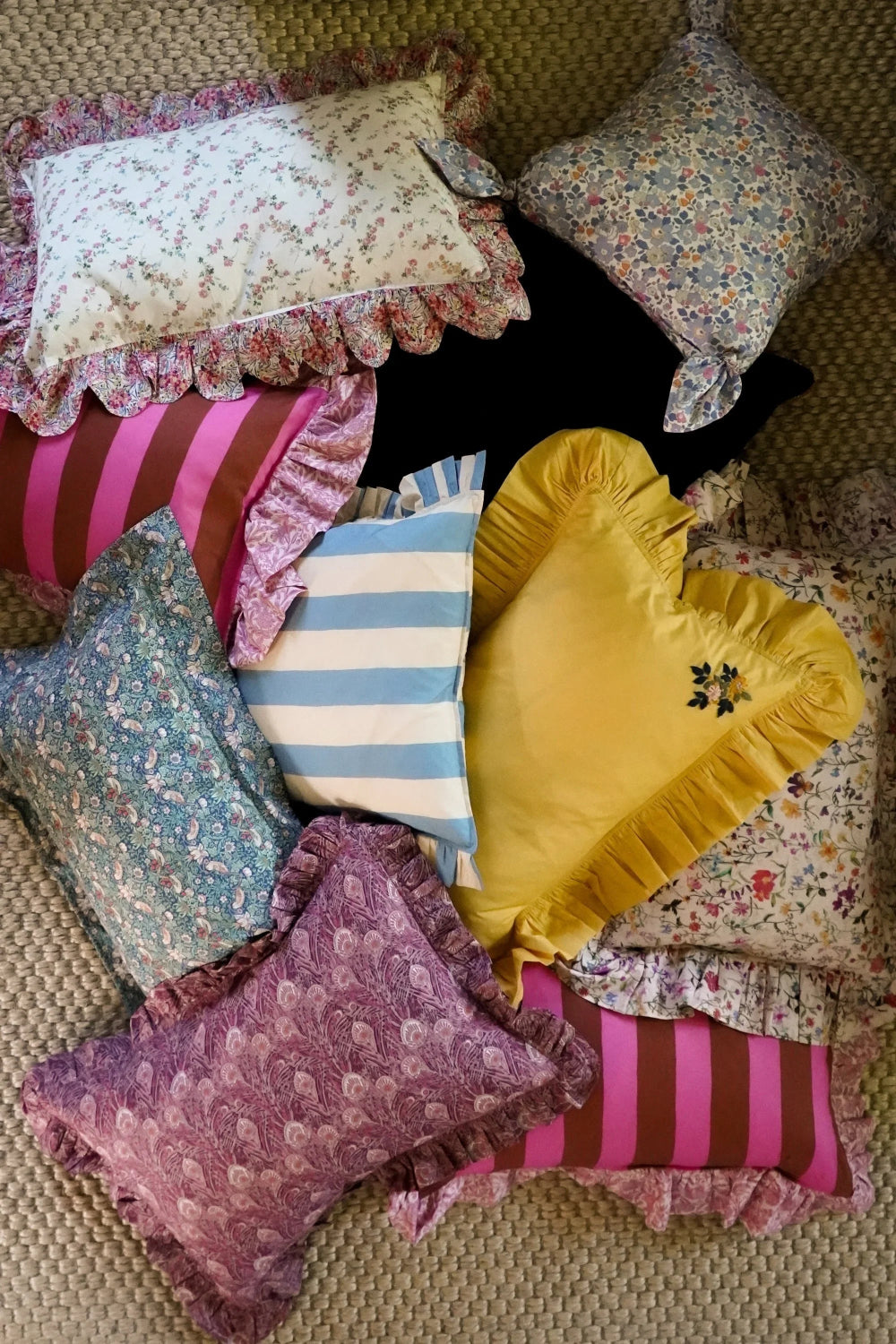 Collection of decorative pillows with various patterns and colours on a textured surface.