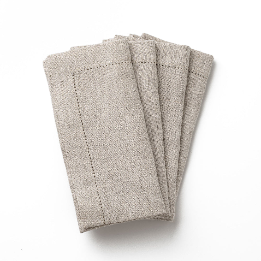 Set of four hemstitched folded beige napkins on a white background