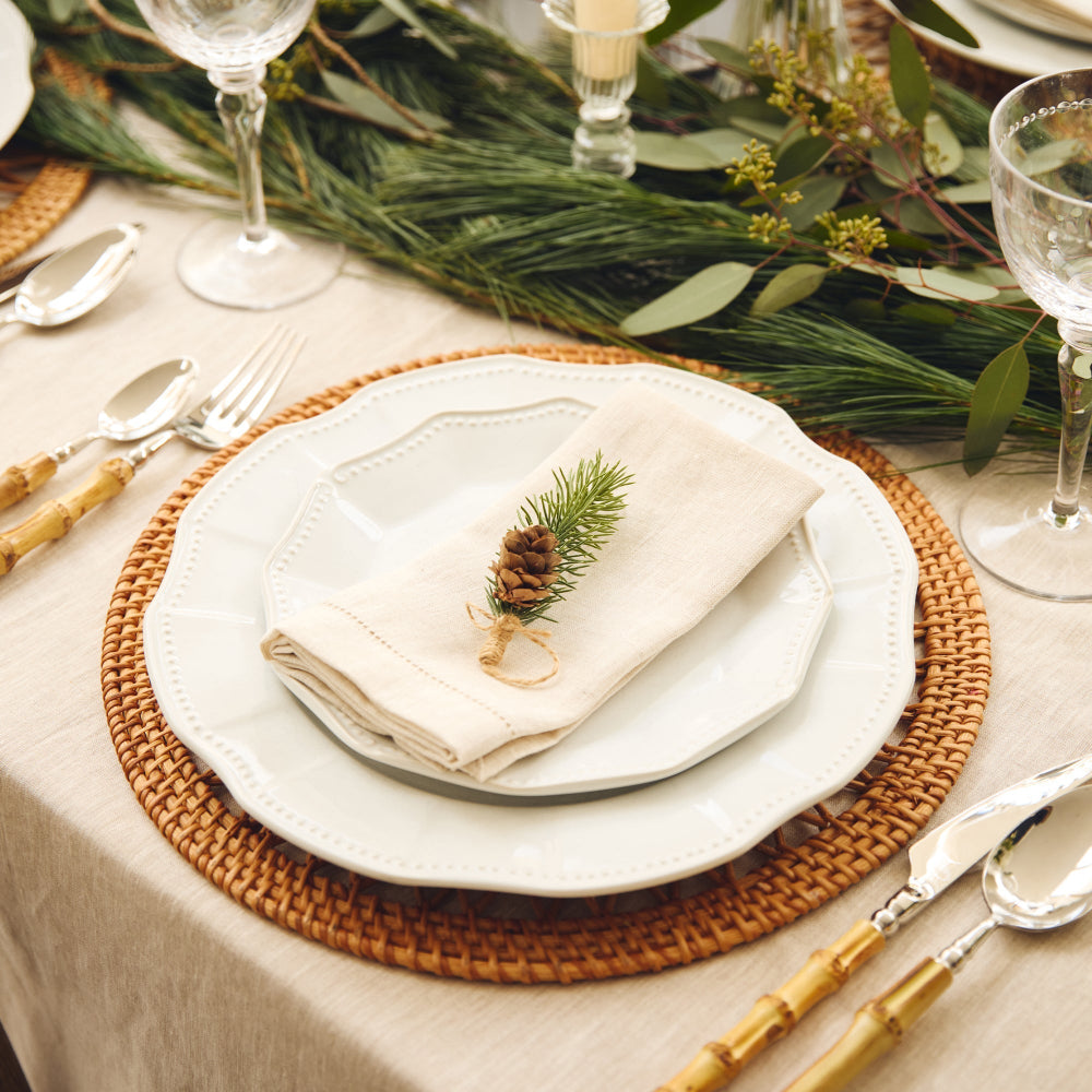 Table setting with white plates, napkins, and christmas decorative elements on a tablecloth.