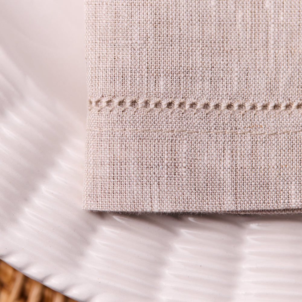 Close-up of beige hemstitched napkins with a woven pattern on a white background