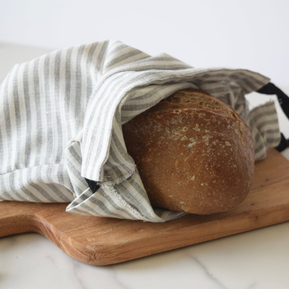 Loaf of bread wrapped in a striped cloth on a wooden cutting board