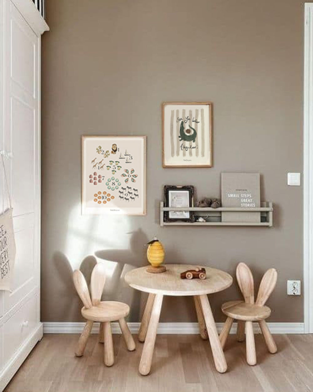 Children's room with wooden table and chairs against a grey wall with framed pictures.