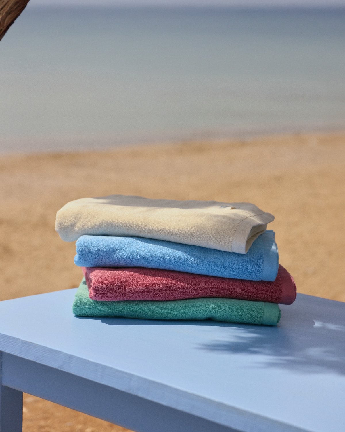 Stack of colourful organic towels on a blue table with a beach background