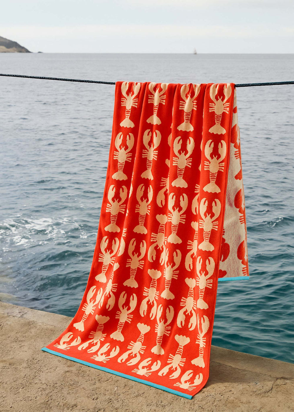Red towel with lobster pattern on a stone ledge by the sea water