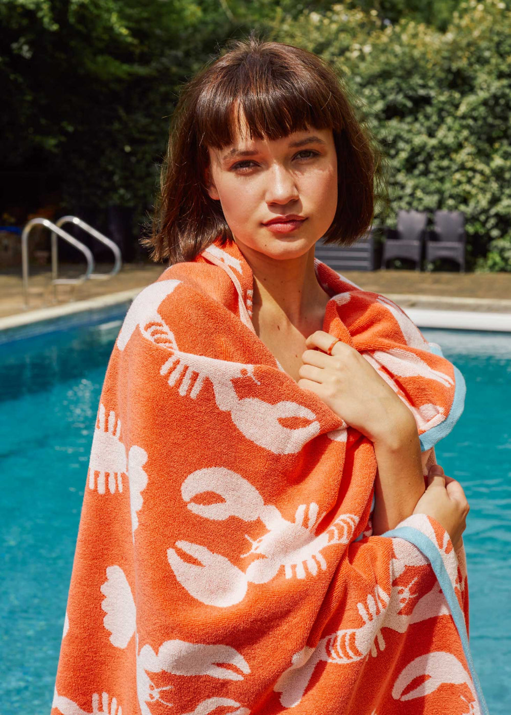 Woman wrapped in an orange towel with white lobster patterns by a pool