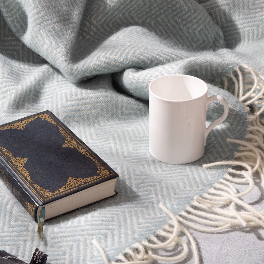 White mug and black book on a textured blanket