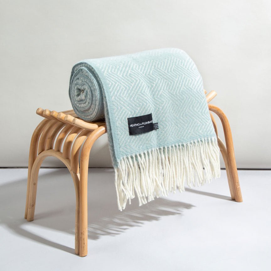 Duck egg blanket with white fringe draped over a wooden stool on a light grey background