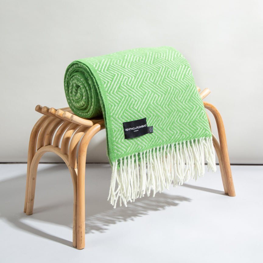 Green blanket with white fringe draped over a wooden stool on a light background