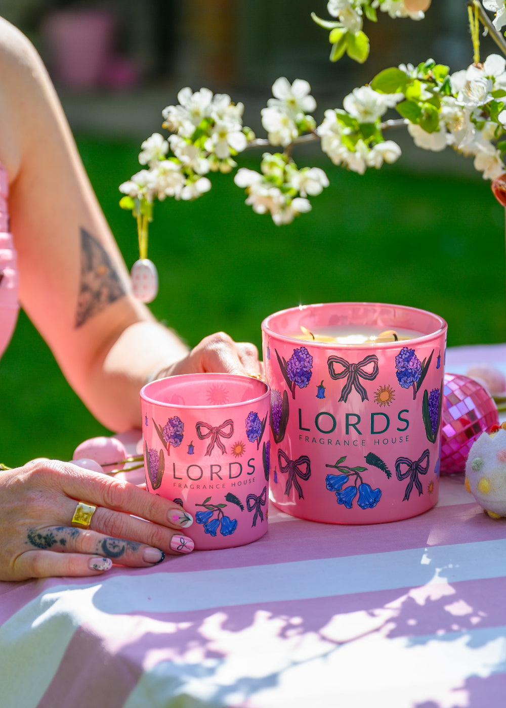 Two pink candles with floral designs on a table outdoors, surrounded by white flowers.