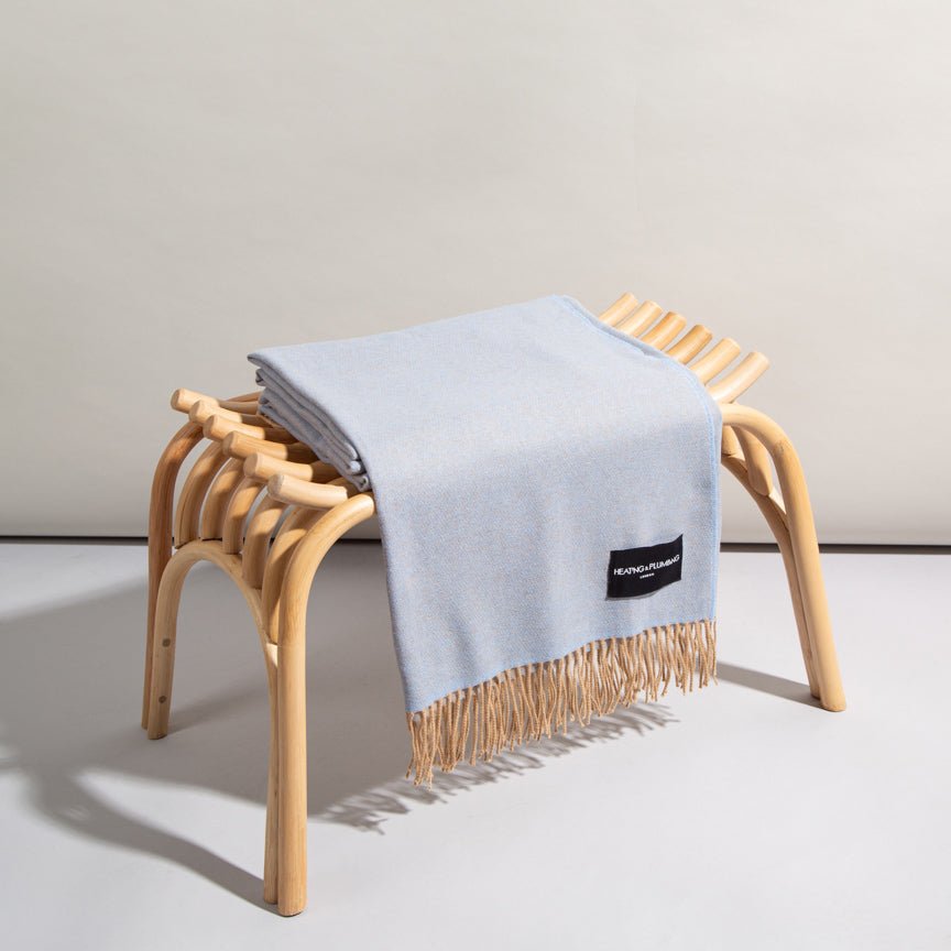 Light blue throw blanket with a brand label draped over a wooden stool on a neutral background