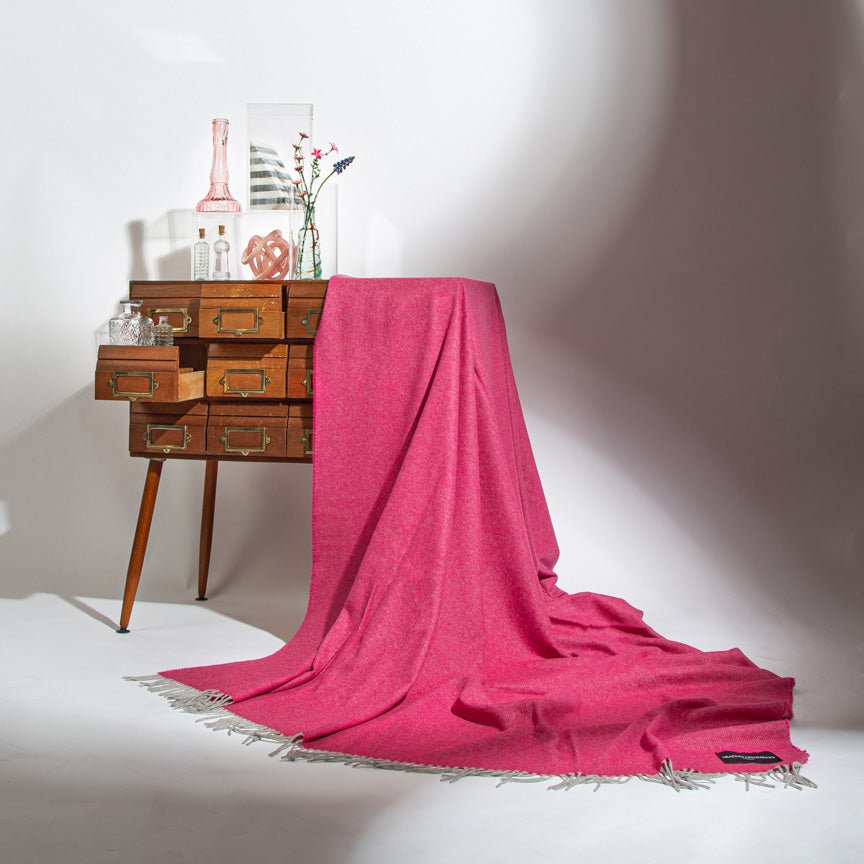 Pink blanket draped over a wooden side table with decorative items on a white background
