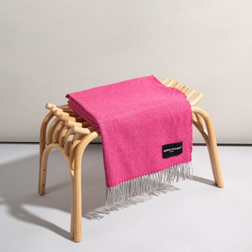 Pink throw blanket with fringe draped over a wooden stool on a light grey background