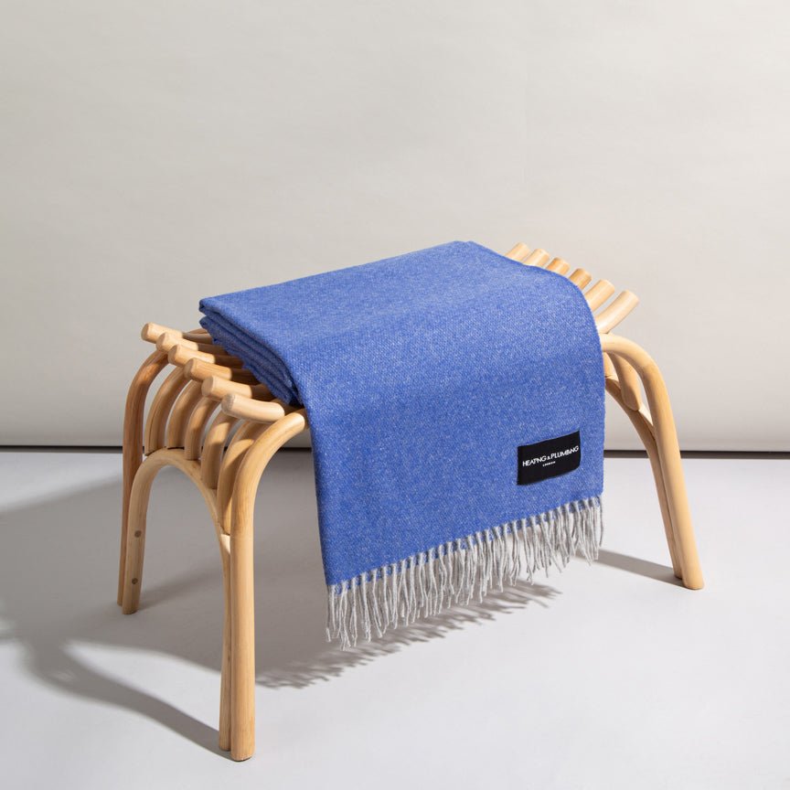 Blue throw blanket draped over a wooden stool on a light grey background