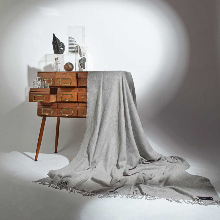 Grey throw blanket draped over a wooden sideboard against a white background
