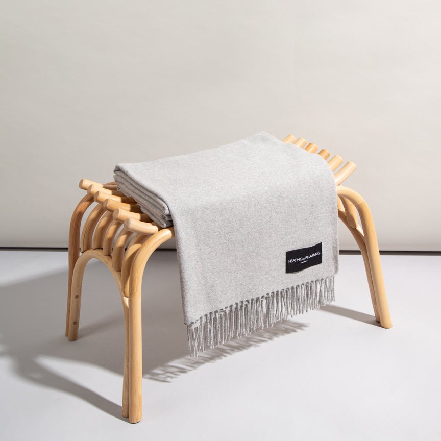 Grey blanket with a brand label draped over a wooden stool against a plain background