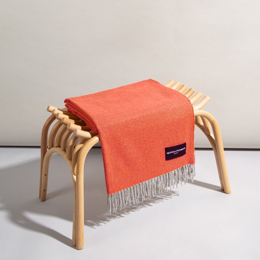Tangerine coloured blanket with a brand label draped over a wooden stool on a light background